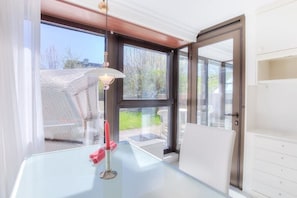 Ein Zimmer mit einem Glastisch, einer roten Kerze und Blick ins Freie durch große Fenster.