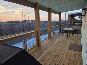 A covered outdoor deck with a table and chairs, overlooking a fenced area. - NEW Charming Cottage in Rockport, Sunset Views, Dog-friendly - Sleeps 6 (Rockport)
