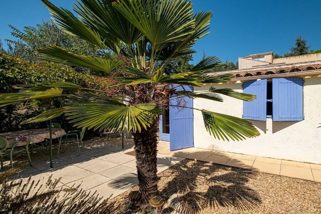 A building with blue shutters, a palm tree, and a patio area with chairs and a table.