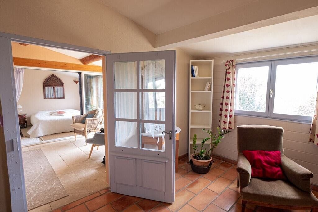 Une pièce comprenant un lit, une chaise, une bibliothèque et une fenêtre avec des rideaux.