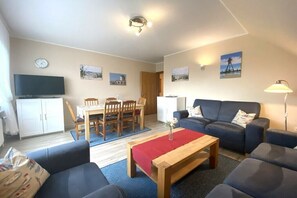 Een woonkamer met een bank, een salontafel, een televisie en een eethoek met stoelen en een tafel.