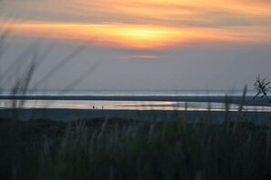 Een strandscène met een zonsondergang, een rustige zee en mensen op de achtergrond.