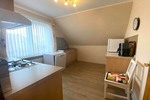 Eine kleine Küche mit einem Gaskochfeld, einem weißen Kühlschrank und einem Holzstuhl mit einer Patchworkdecke.