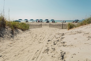A sandy beach path leading to beach umbrellas and chairs, with a wooden fence in the middle. - North Myrtle Beach | Marsh Escape | Pool & Beach Access | 2BR Villa (North Myrtle Beach)