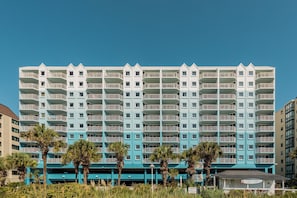 A multi-story hotel with balconies, a flat roof, and a parking area in front. - North Myrtle Beach | Marsh Escape | Pool & Beach Access | 2BR Villa (North Myrtle Beach)