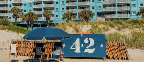 Un edificio frente al mar con balcones, un área de sillas de playa y un letrero con el número 42.