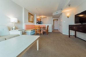 A living room with a sofa, a dining table, and chairs, a kitchen area with appliances, and a TV on the wall. - North Myrtle Beach | Marsh Escape | Pool & Beach Access | 2BR Villa (North Myrtle Beach)