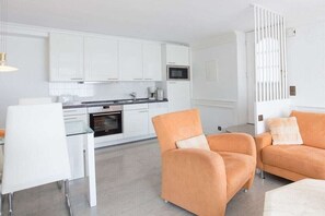 A modern kitchen with white cabinets, a microwave, and a dining area with a white table and chairs. - Holiday apartment in Sylt with 1 bedroom (Wenningstedt)