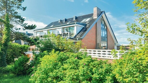 Une maison moderne avec un toit en pente, de grandes fenêtres et une façade en briques.