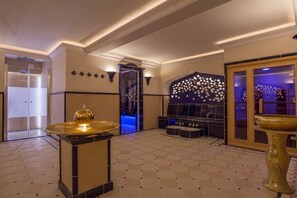 En rymlig entréhall med modern design, med en central sittgrupp, en dekorativ vägg med ett stjärnmönster och en stor, gyllene fontän.