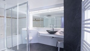 Une salle de bain moderne avec une douche à l’italienne en verre, des toilettes blanches, un lavabo noir avec un receveur, et un grand miroir au-dessus du meuble-lavabo.