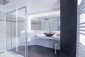 Ett modernt badrum med en duschavdelning med glasväggar, en vit toalett, en svart tvättställskommod med en fristående tvättskål och en stor spegel ovanför tvättstället.