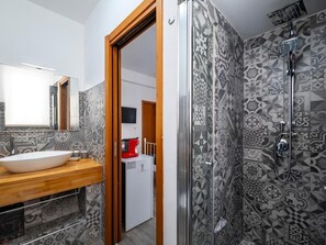 Une salle de bain avec un grand miroir, un lavabo blanc, une douche avec une porte en verre et des carreaux décorés.