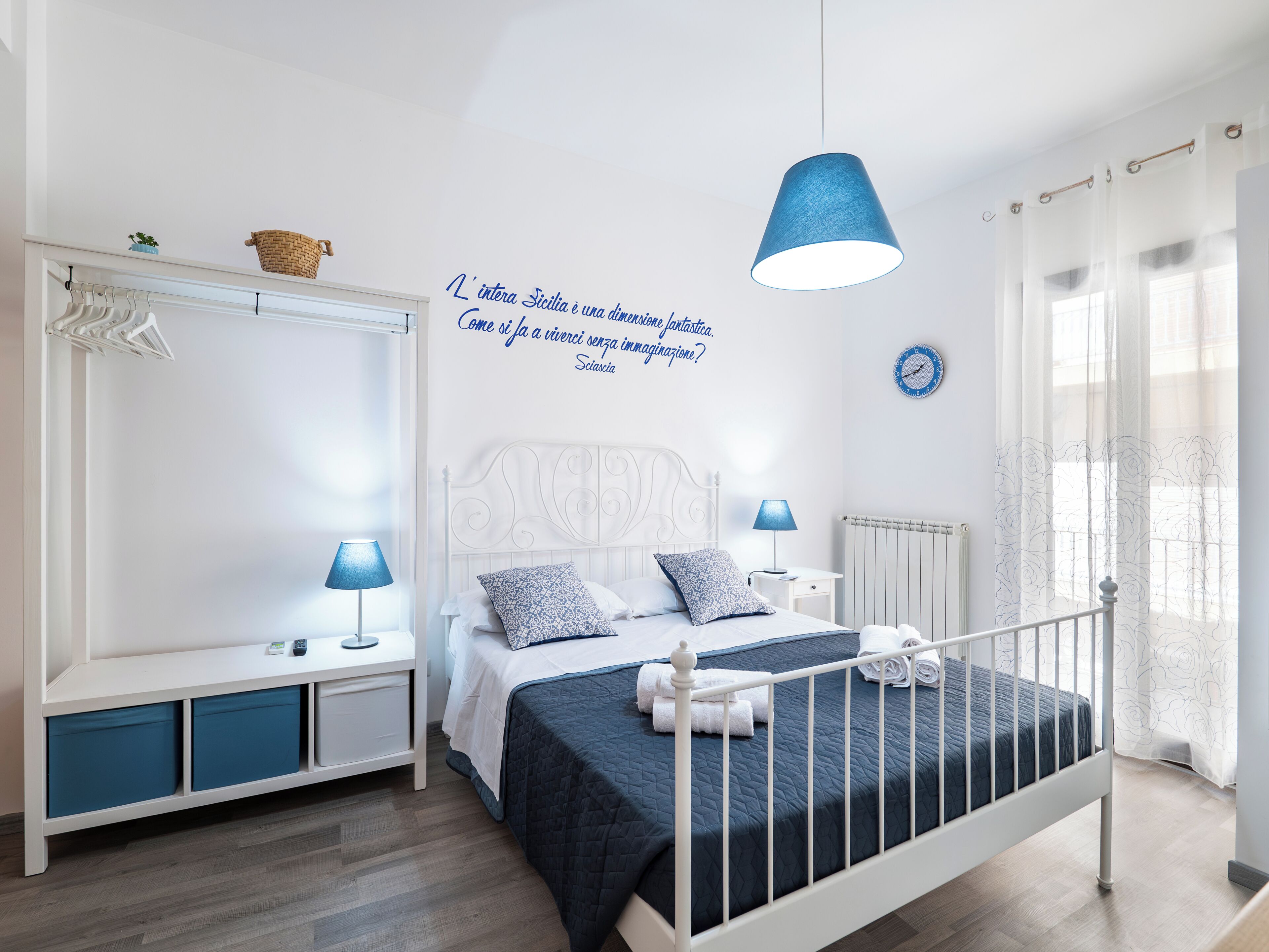 Ein Schlafzimmer mit Bett, Nachttischen, einem Kleiderschrank, einer Hängeleuchte und einer Wanduhr.
