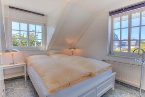 Ein Schlafzimmer mit Bett, Nachttisch, Lampe, Fenster und Heizkörper.