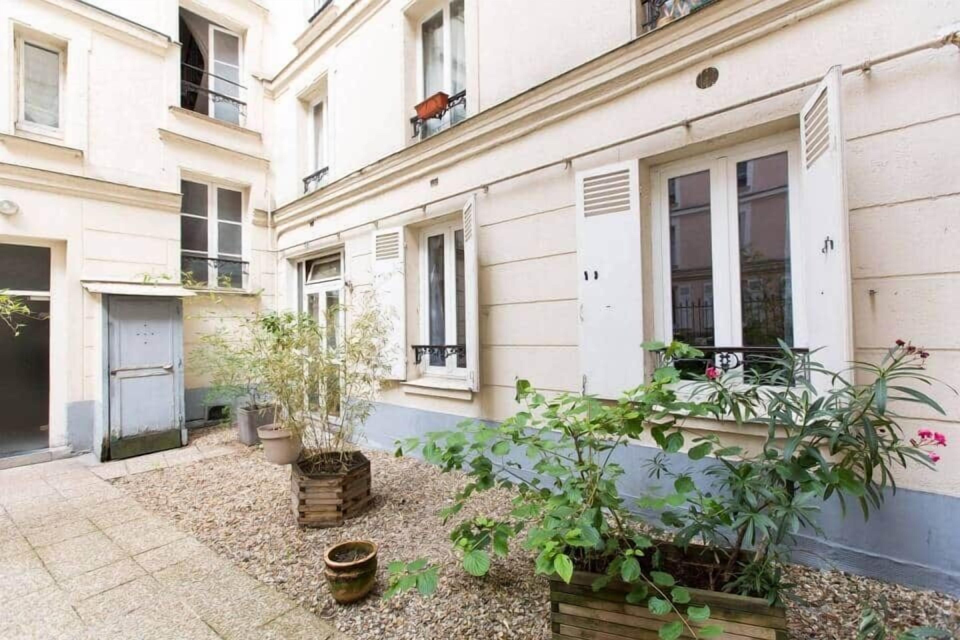 A courtyard with potted plants, a door, and windows.