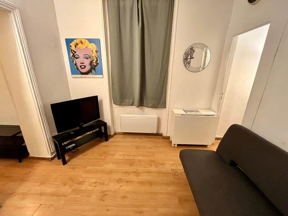 Ein Wohnzimmer mit Flachbildfernseher, einer Couch, einem kleinen Tisch und einer Wanduhr.