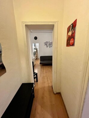 Ein schmaler Flur mit Holzboden führt zu einem Wohnbereich mit einer Couch und einer Wanddekoration.
