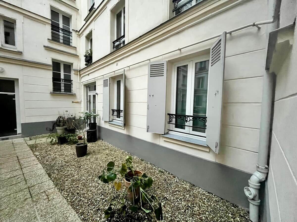 A building facade with multiple windows, some with shutters, and a gravel courtyard with potted plants.