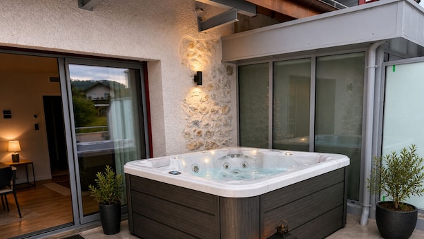 A hot tub in a modern outdoor setting with a stone wall, a glass door leading to a patio, and a welcome mat. - Résidence le 1900 (VULBENS)