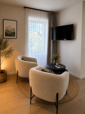 A modern living room with two armchairs, a flat-screen TV, a potted plant, and a framed picture on the wall.