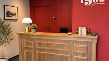 A reception desk with a red wall, a framed picture, a potted plant, and a lamp.