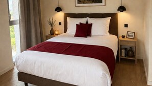 Quarto com cama grande, mesa de cabeceira, luminária na parede e quadro acima da cama.