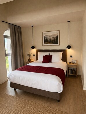 Un dormitorio con una cama grande, una mesita de noche, una lámpara de pared y un cuadro enmarcado sobre la cama.