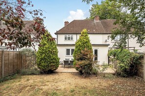 A two-story house with a tiled roof, a fenced backyard, and a patio area with outdoor furniture. - Surrey 5-Bed Home for Groups & Business Stays - Pass the Keys (Addlestone)