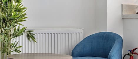 A room with a blue armchair, a small round table, a radiator, and a fire extinguisher on the wall.