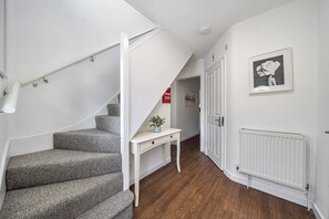 A staircase with a white handrail, a small white table with a plant, and a framed picture on the wall.