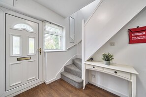 A staircase leading to a landing with a white console table and a red fire safety document holder. - Surrey 5-Bed Home for Groups & Business Stays - Pass the Keys (Addlestone)