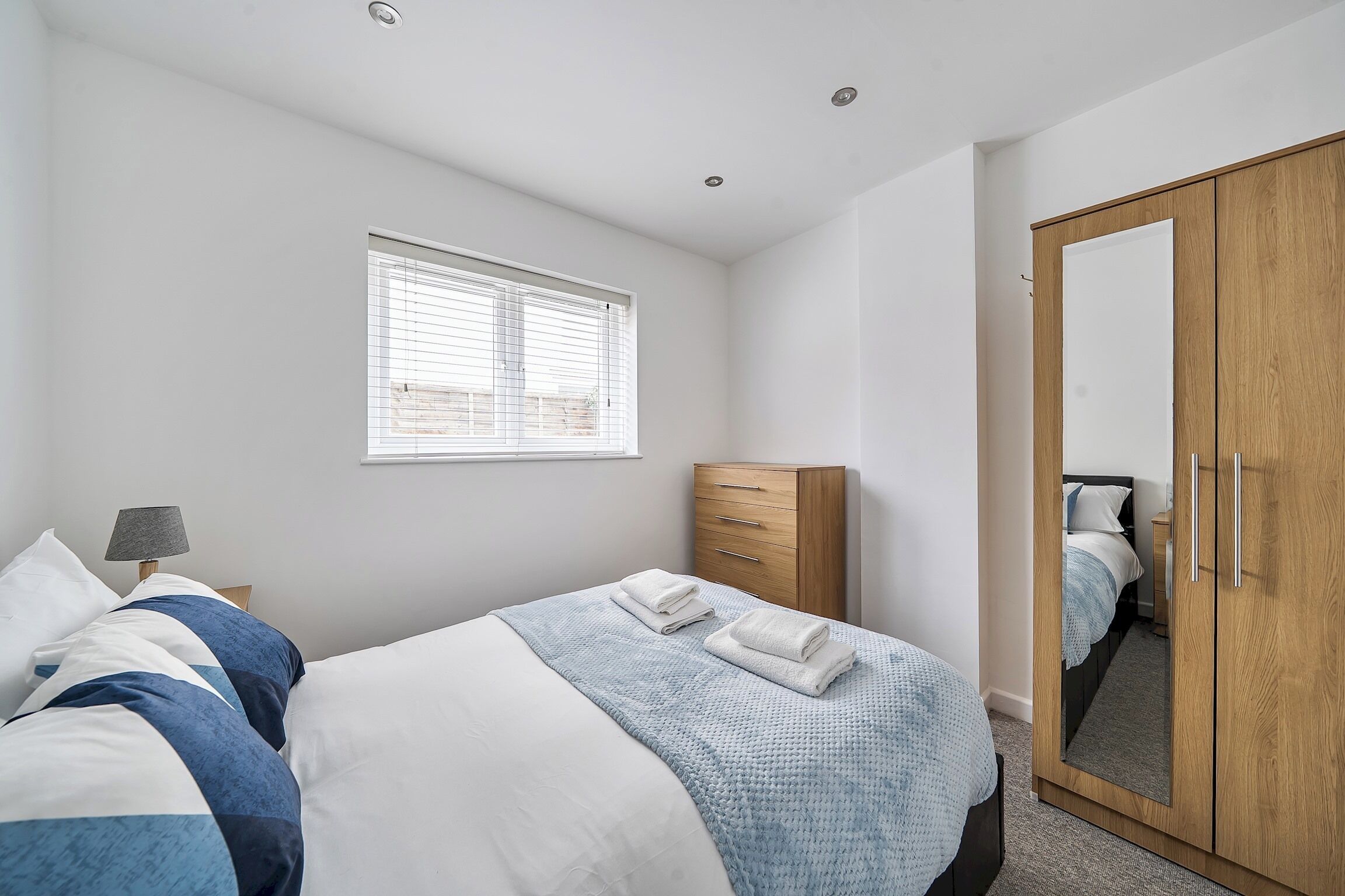 Un dormitorio con cama, armario, ventana con persianas y espejo.