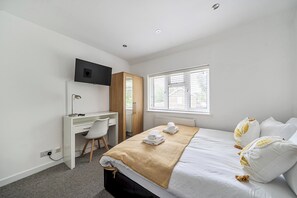 A hotel room with a bed, a desk, a chair, a television, and a window with blinds.