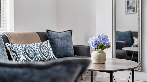 En moderne stue med sofa, sofabord og en vase med blomster.