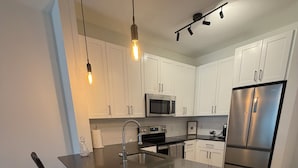 Een moderne keuken met een centraal eiland, roestvrijstalen apparatuur en hangende verlichting.
