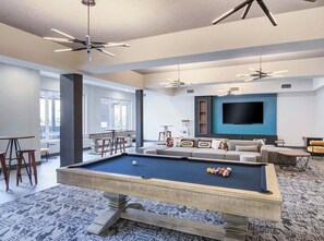A pool table in a modern living room with a large TV, comfortable seating, and a ceiling fan.