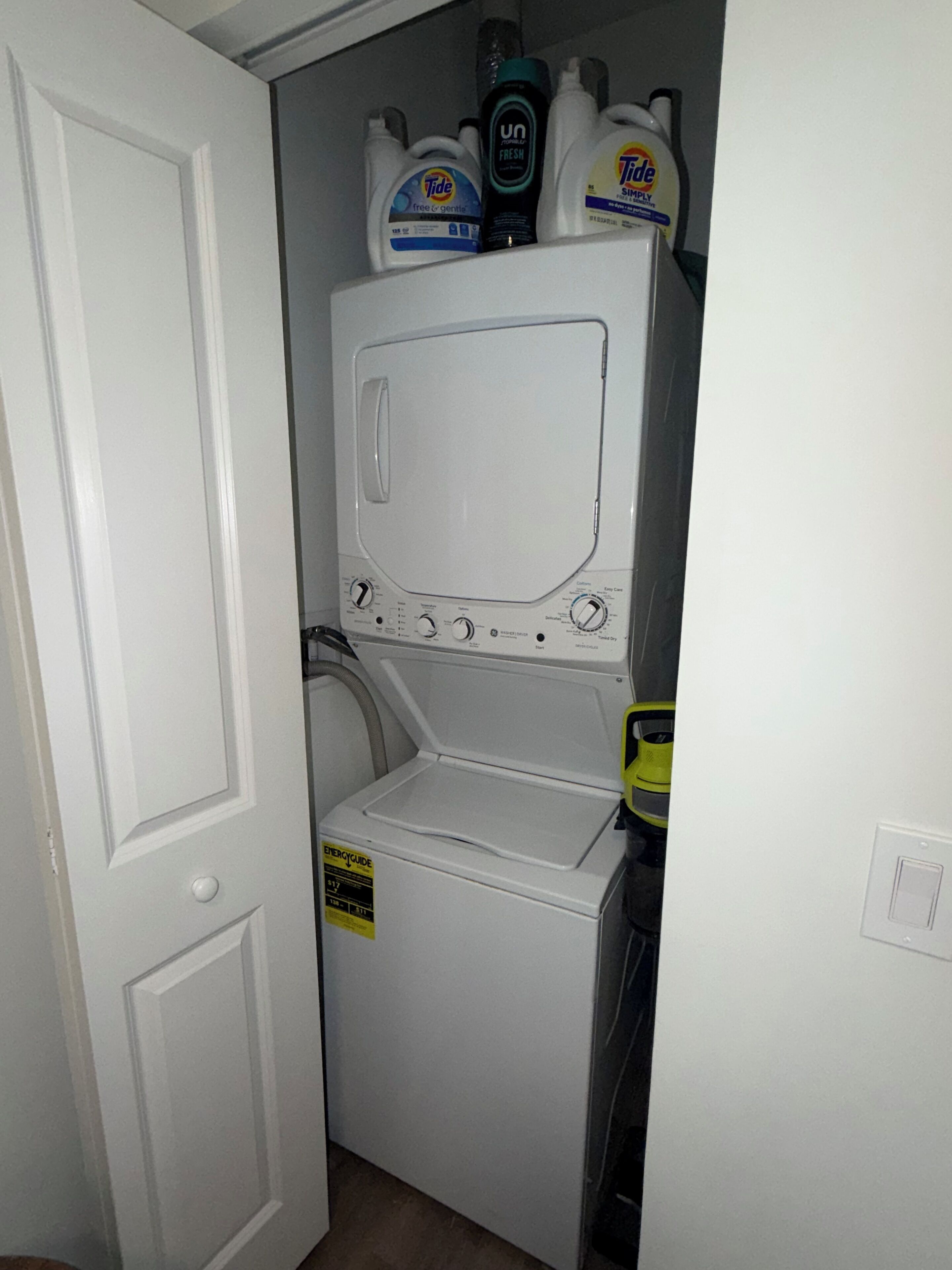 Une petite buanderie comprenant un lave-linge et un sèche-linge, une porte et des bouteilles de lessive posées sur le dessus.