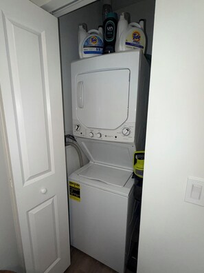 A compact laundry room with a washing machine and dryer, a door, and detergent bottles on top.
