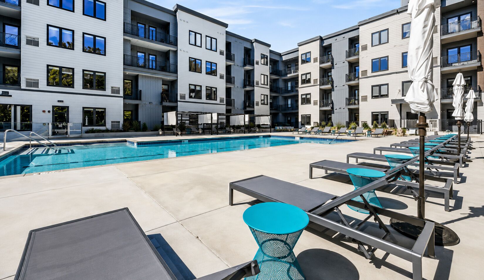 A rooftop pool area with lounge chairs and umbrellas, surrounded by modern apartment buildings.