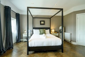 A four-poster bed with white linens, a nightstand with a lamp, a small table with a mirror, and a framed picture on the wall. - Elegant Georgian townhouse to sleep 8, town centre - Pass the Keys (Shrewsbury)