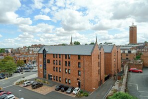 A multi-story brick building with a flat roof, a parking lot with several cars, and a clock tower in the background. - Elegant Georgian townhouse to sleep 8, town centre - Pass the Keys (Shrewsbury)
