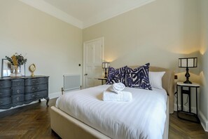 A neatly made bed with a rolled towel, a dresser with drawers, a radiator, and two bedside lamps. - Elegant Georgian townhouse to sleep 8, town centre - Pass the Keys (Shrewsbury)