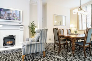 Uma sala de jantar com lareira, poltronas listradas, uma mesa de jantar de madeira e um espelho sobre ela.