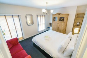 Een hotelkamer met een bed, een rode stoel, een houten garderobe en een kroonluchter.