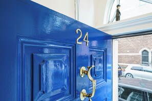 A blue door with the number 24, a brass door knocker, and a window above showing a brick building and parked cars. - Charlie Chaplin House - A Historic Memorable Stay - Pass the Keys (Belfast)