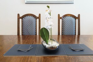 Een eettafel met een vaas witte orchideeën, twee stoelen met gestreepte kussens en een zwarte placemat.
