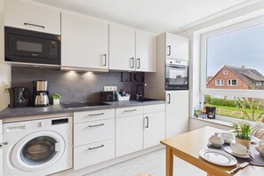 A modern kitchen with a washing machine, microwave, and oven. - Holiday apartment Gorch Fock 18 (Langeoog)