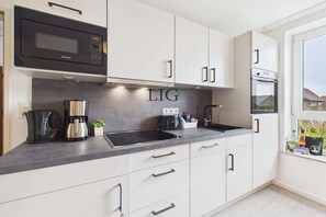 A modern kitchen with white cabinets, a black microwave, a coffee maker, and a sink. - Holiday apartment Gorch Fock 18 (Langeoog)