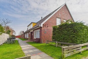 A residential property with a brick house, a pathway leading to the entrance, and a wooden fence. - Holiday apartment Gorch Fock 18 (Langeoog)